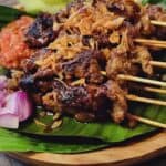 a plate of beef satay with tomato chili condiments and cucumber slices.