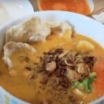 A bowl of soto tangkar in with rice at the background.