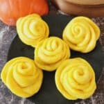 Rose Pumpkin Mantou on a black plate with pumpkin next to it.