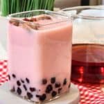 a glass of rose milk tea with tapioca pearls inside.