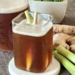 A glass of cold red ginger drink with two stalks of lemongrass.