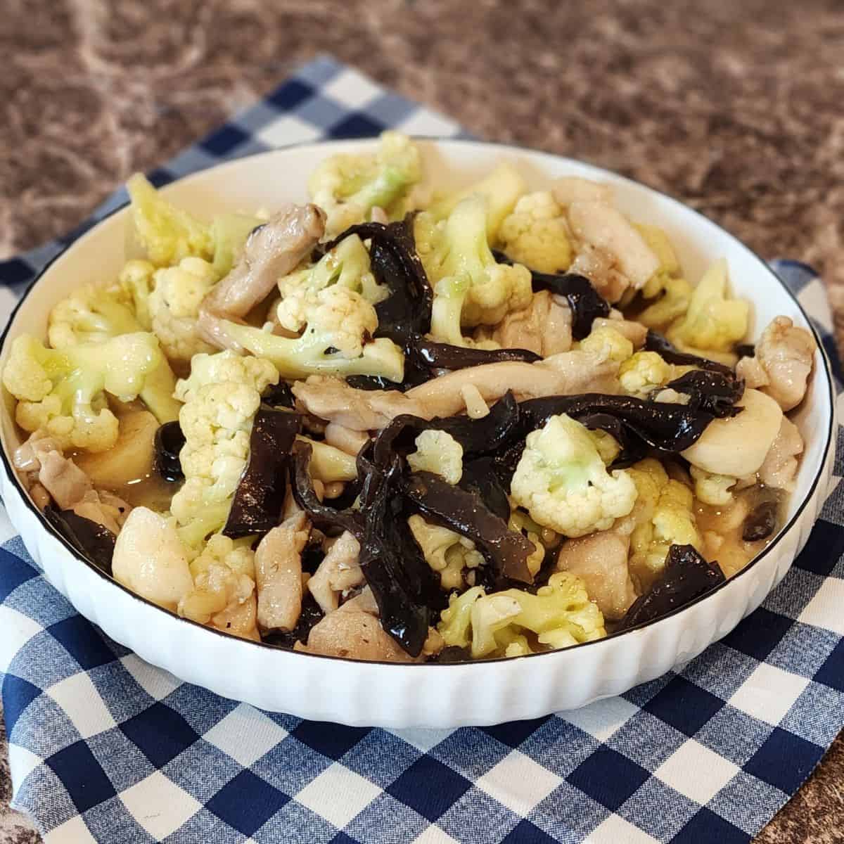 A plate of Asian kikurage cauliflower chicken on a blue and white napkin.
