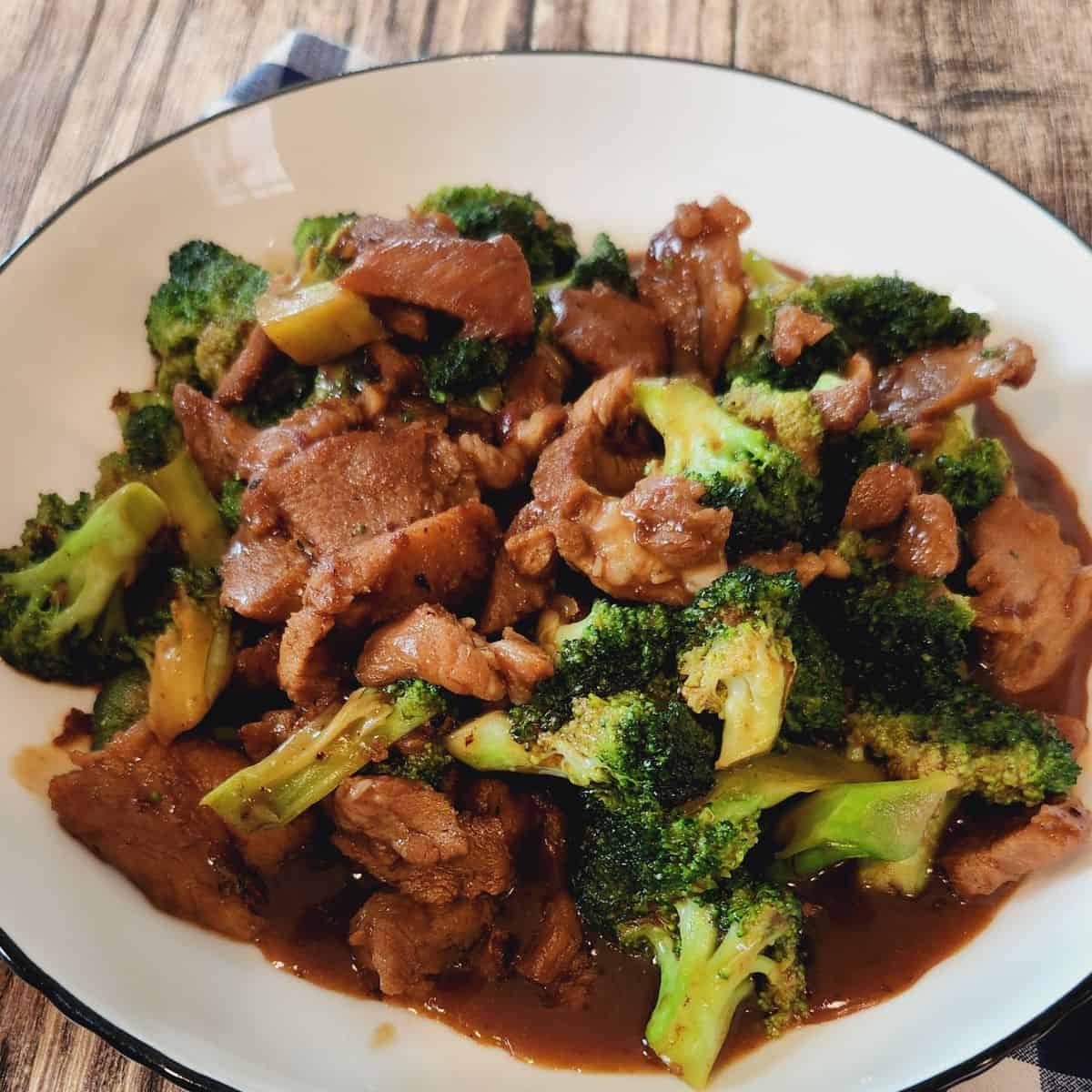 A plate of pork and broccoli stir fry on wooden table.