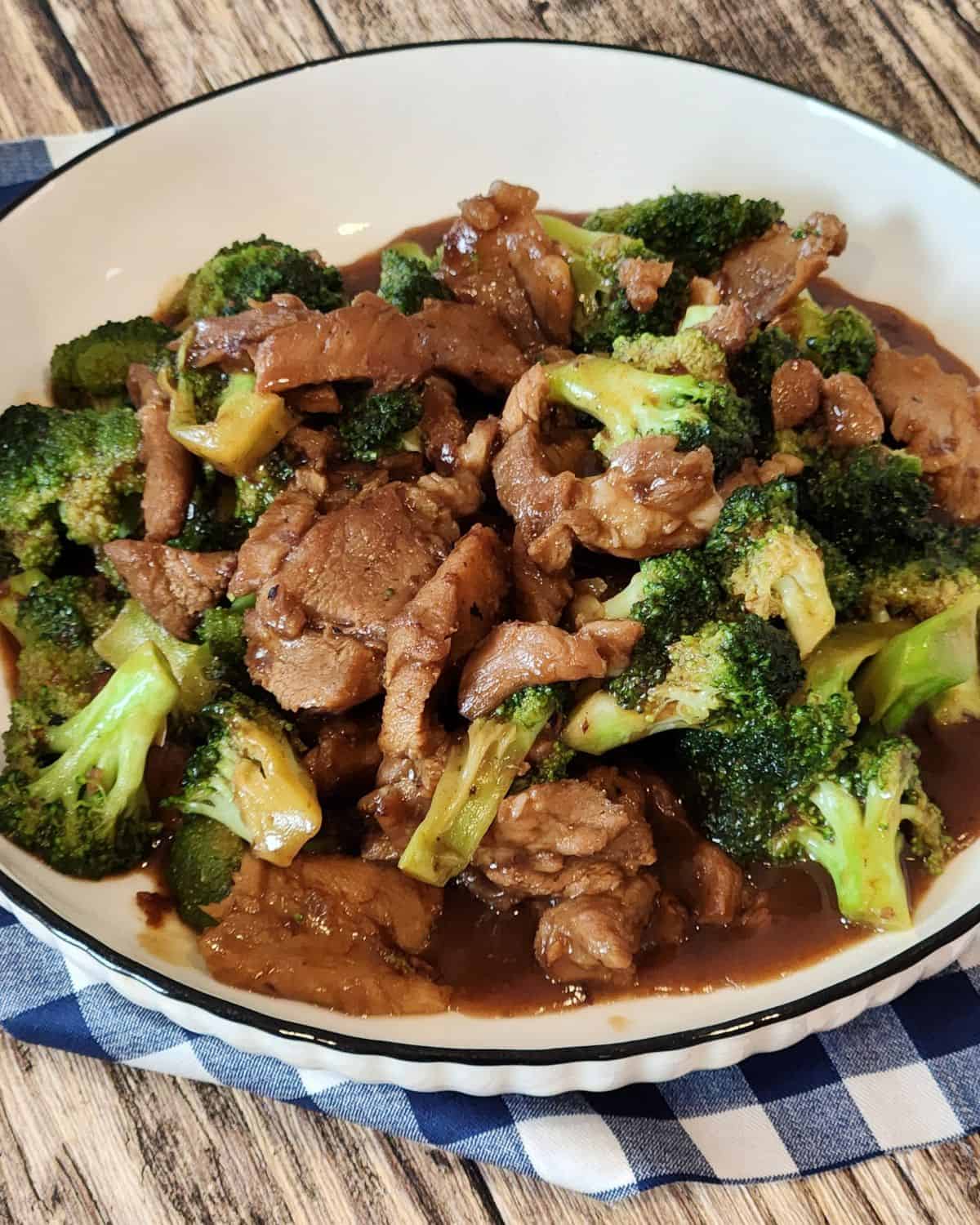 A plate of pork and broccoli stir fry on a blue and white napkin.