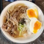 A photo of Yoshinoya gyudon beef on fluffy white rice and a soft-boiled egg cut in half.