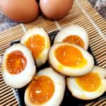Ajitsuke tamago or ramen eggs on a black plate and wooden tray.