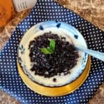A bowl of pulut hitam porridge with coconut sauce on a golden plate and blue and white cloth.
