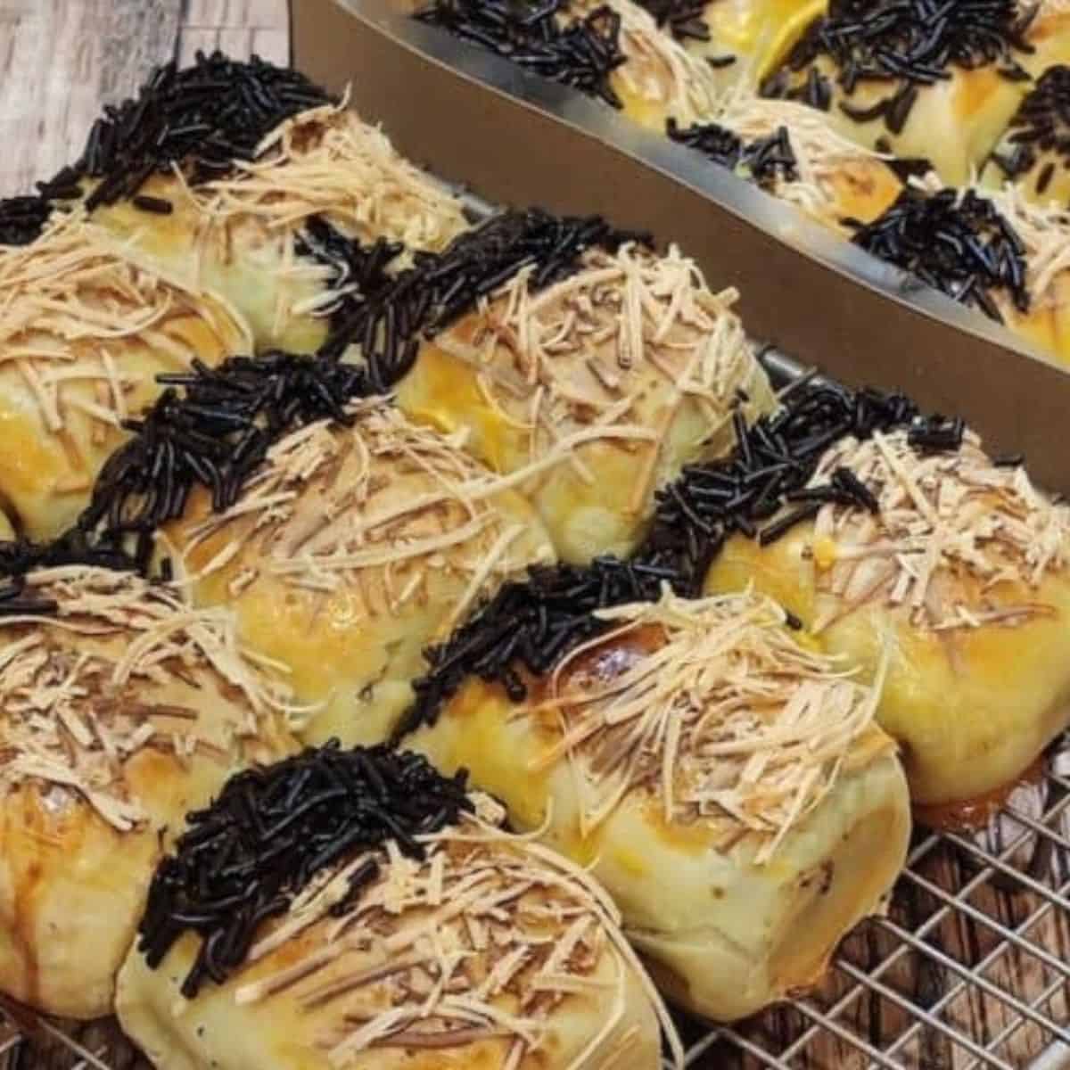Several bolen pisang lined up on a cooling rack next to a box of bolen pisang.