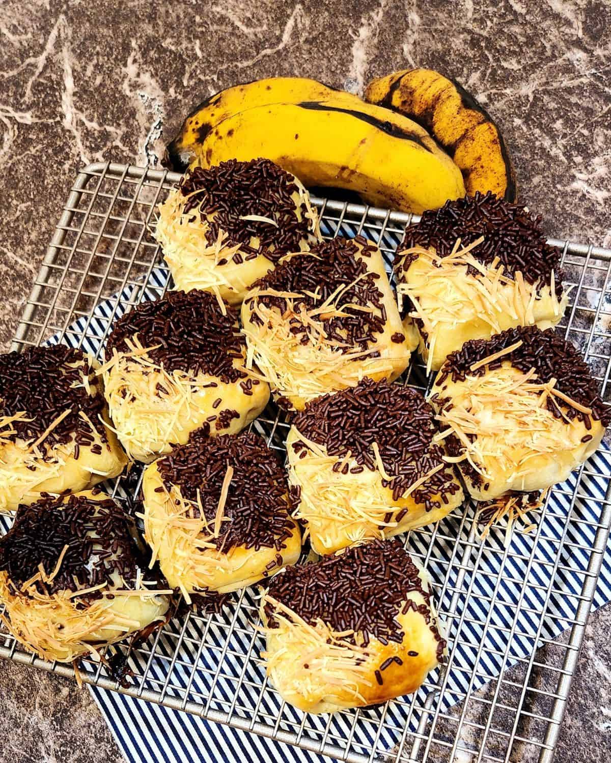 Several bolen pisang lined up on a cooling rack next to two bananas. 