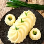 Three pieces of Gluten Free Corn pudding on a black plate with pandan leaves as decoration.