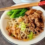 A bowl of minced pork noodles with vegetables and chopsticks.