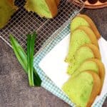Pandan Cake slices on a white plate next to a few pandan leaves.