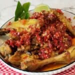 A plate of Ayam Balado garnished with lime leaves and a wedge of lime on red white cloth.
