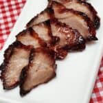 Char Siu Roast Pork slices on a long white plate on red white table cloth.