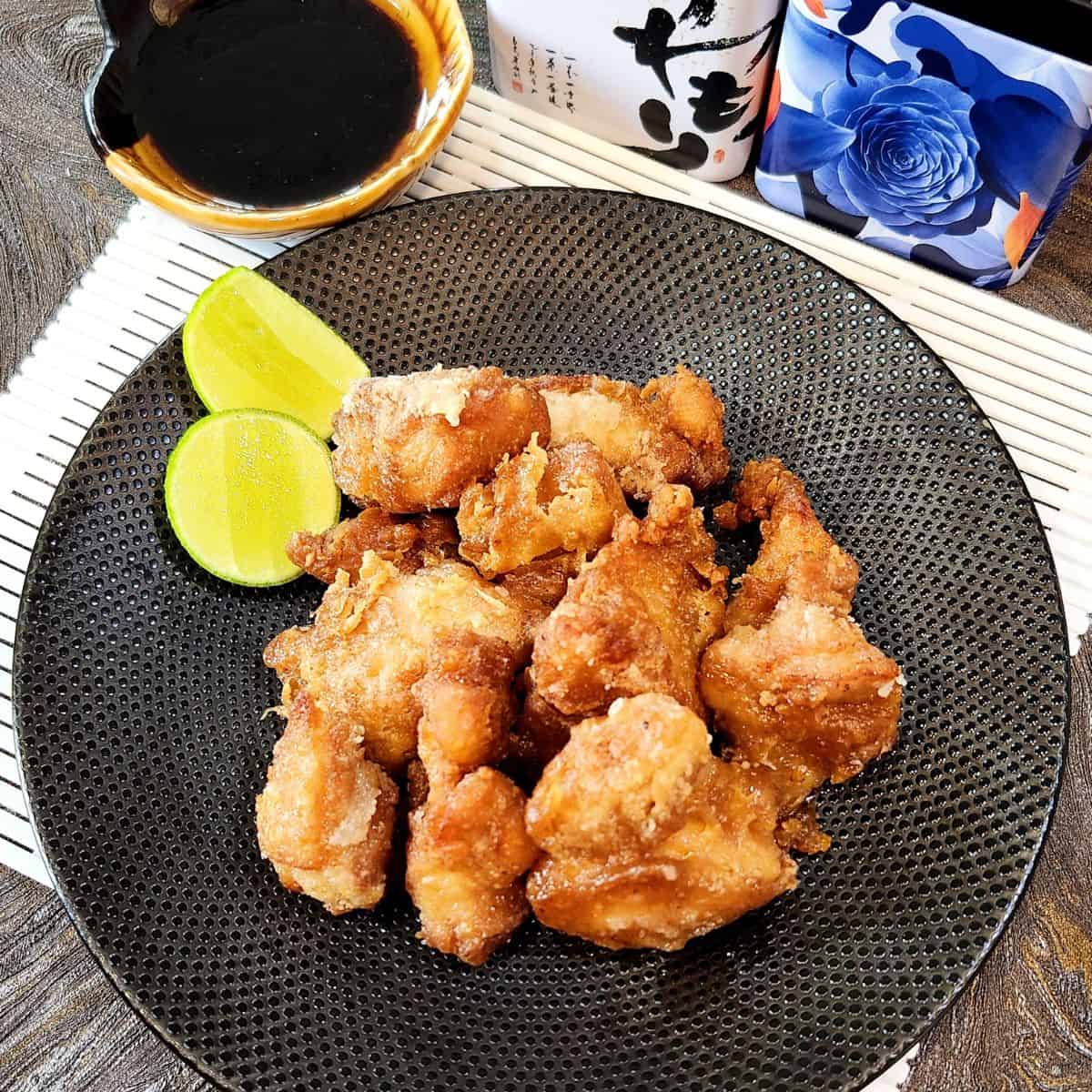 Chicken karaage dish on a black plate with some lime weges and chopsticks.
