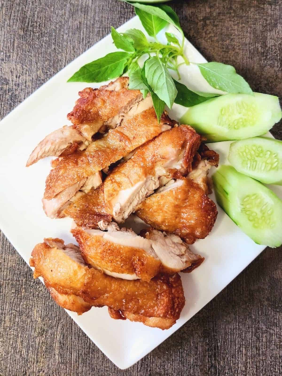 Flourless fried chicken slices on a white plate with some cucumber slices and basil leaves.