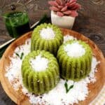 Three Kue Apem Pandan on a wooden plate with grated coconut.