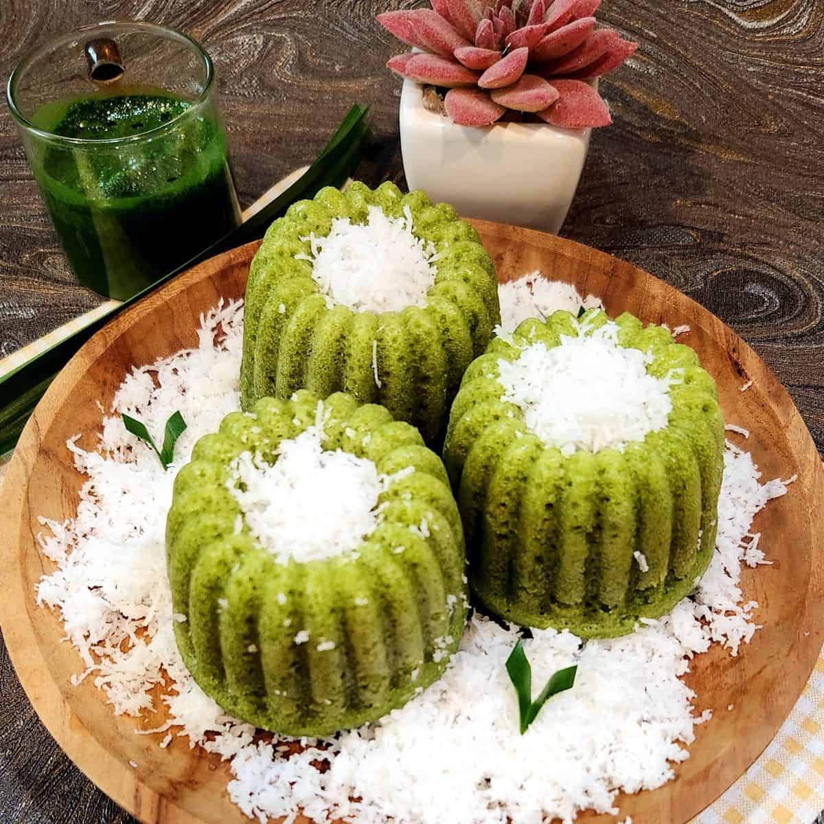 Three Kue Apem Pandan on a wooden plate with grated coconut.