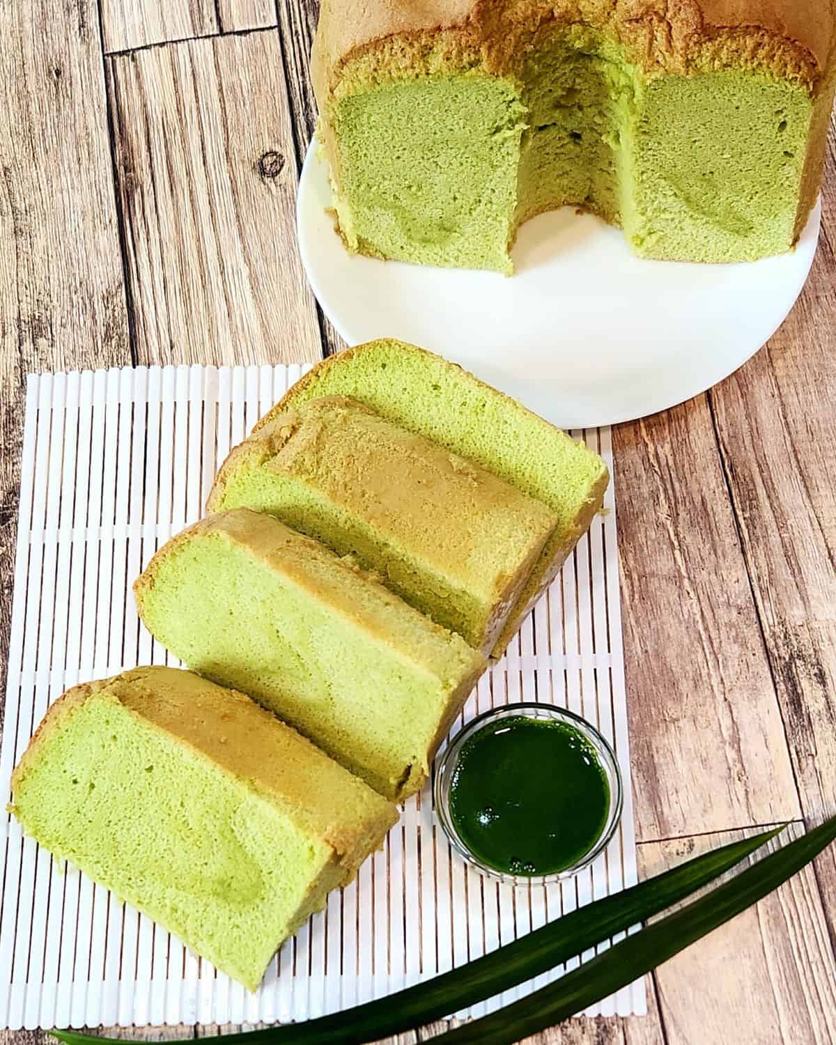 A few slices of pandan chiffon cake on white plastic tray with a cup of pandan extract next to it.