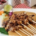 A plate of chicken satay with peanut sauce, pickles, and fried shallots.