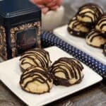 A plate of coconut macaroon with chocolate with tea box behind.