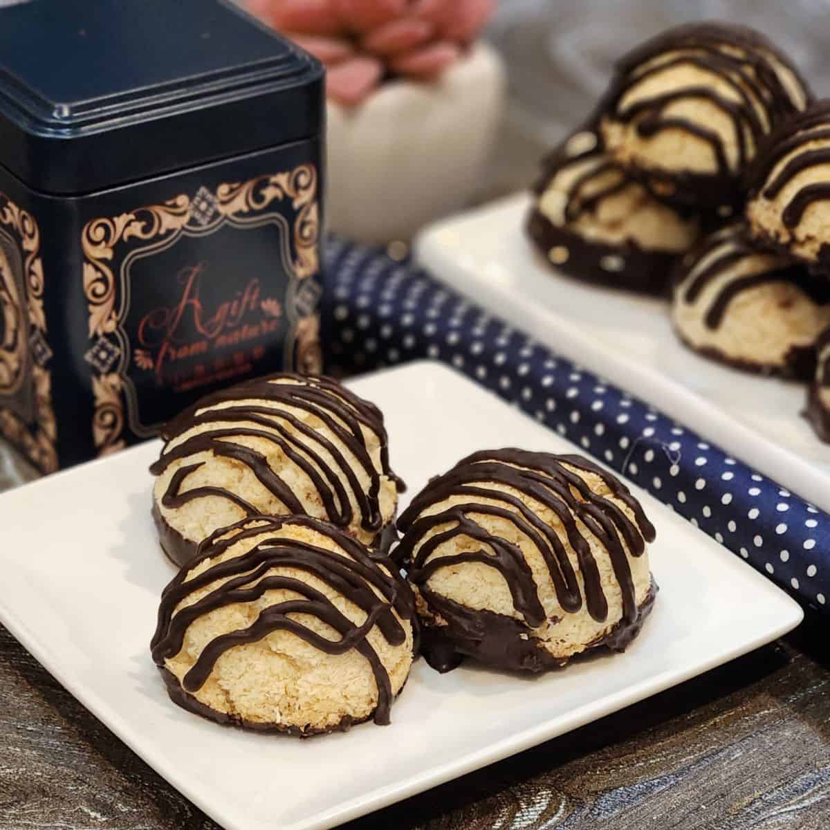 A plate of coconut macaroon with chocolate with tea box behind.