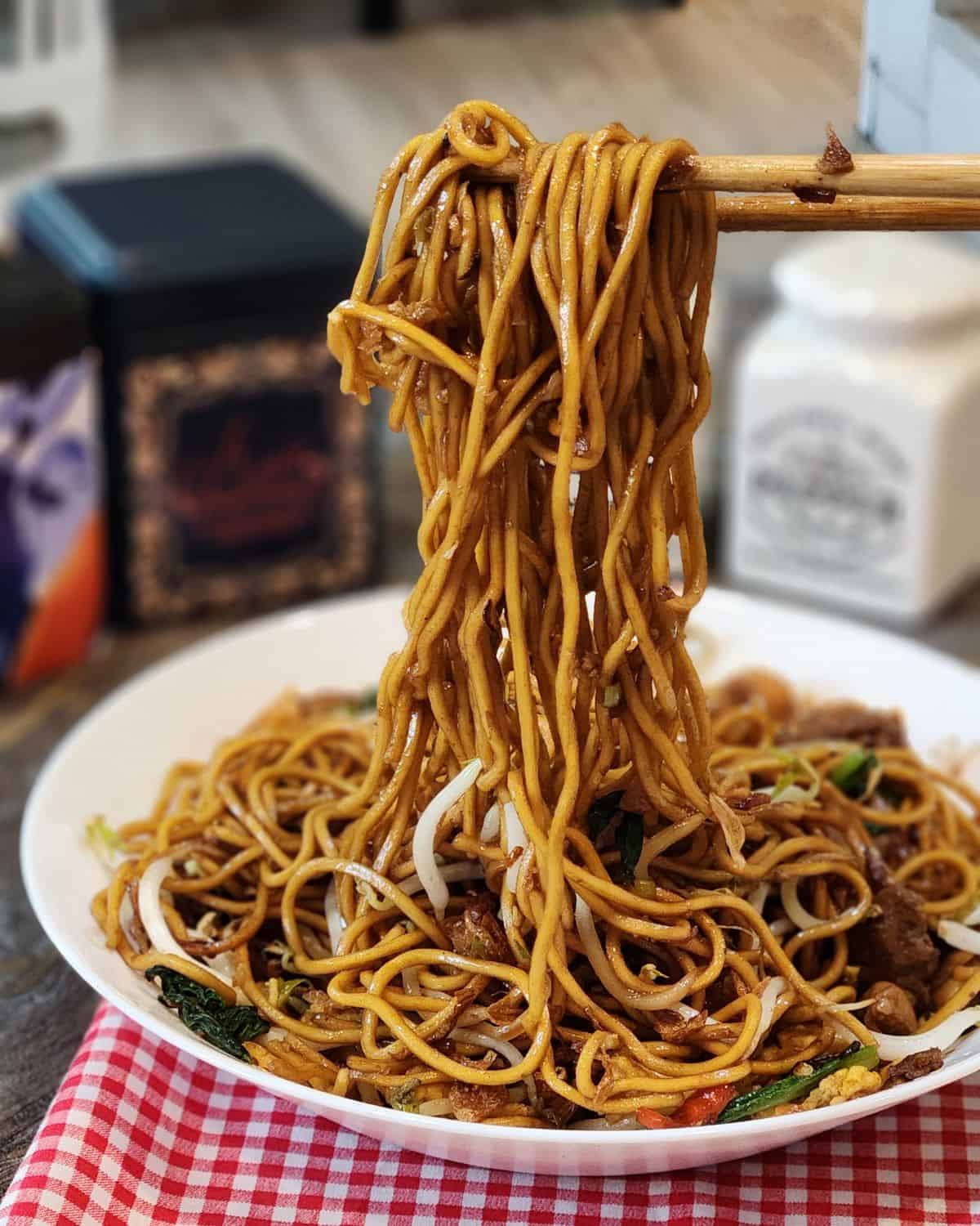 A pair of chopsticks holding mie goreng in the air.