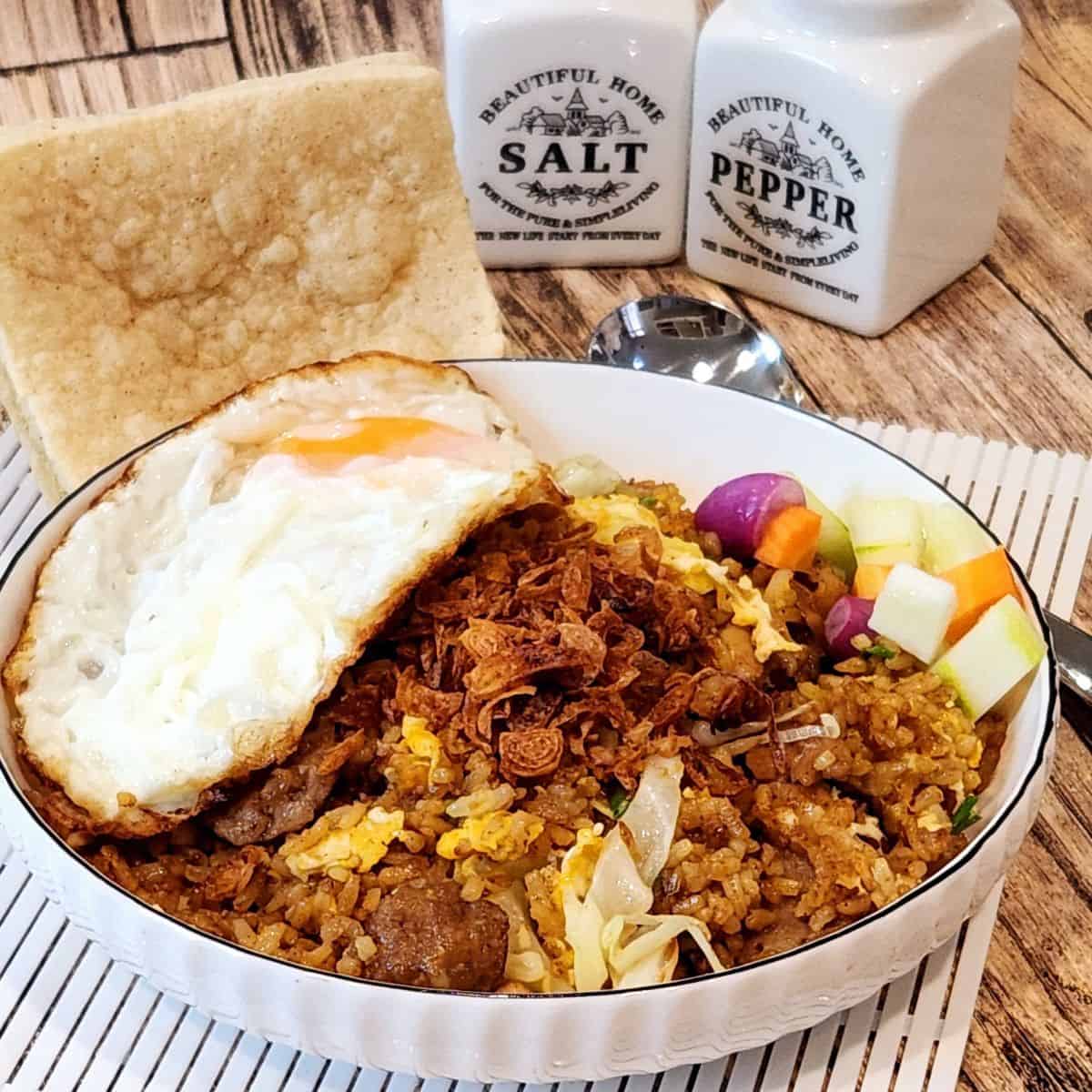 A plate of nasi goreng kampung with sunny side up egg and some pickles.