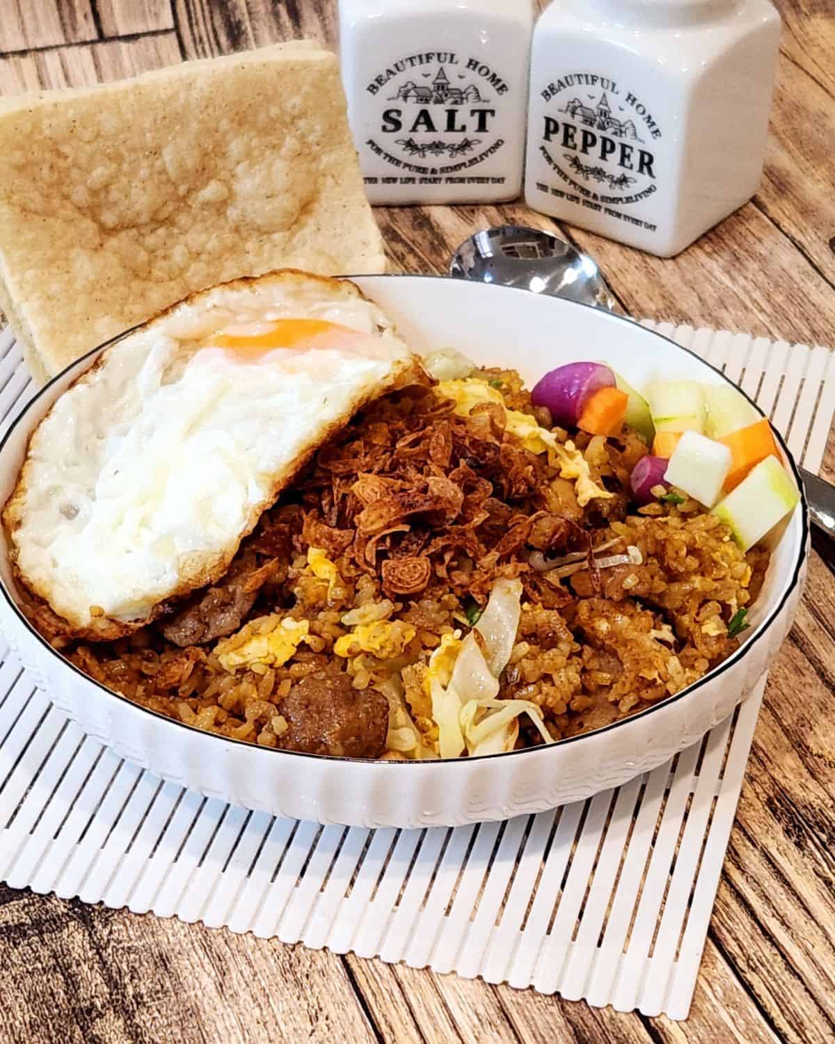 A plate of nasi goreng kampung with pickles, sunny side-up, and cracker.