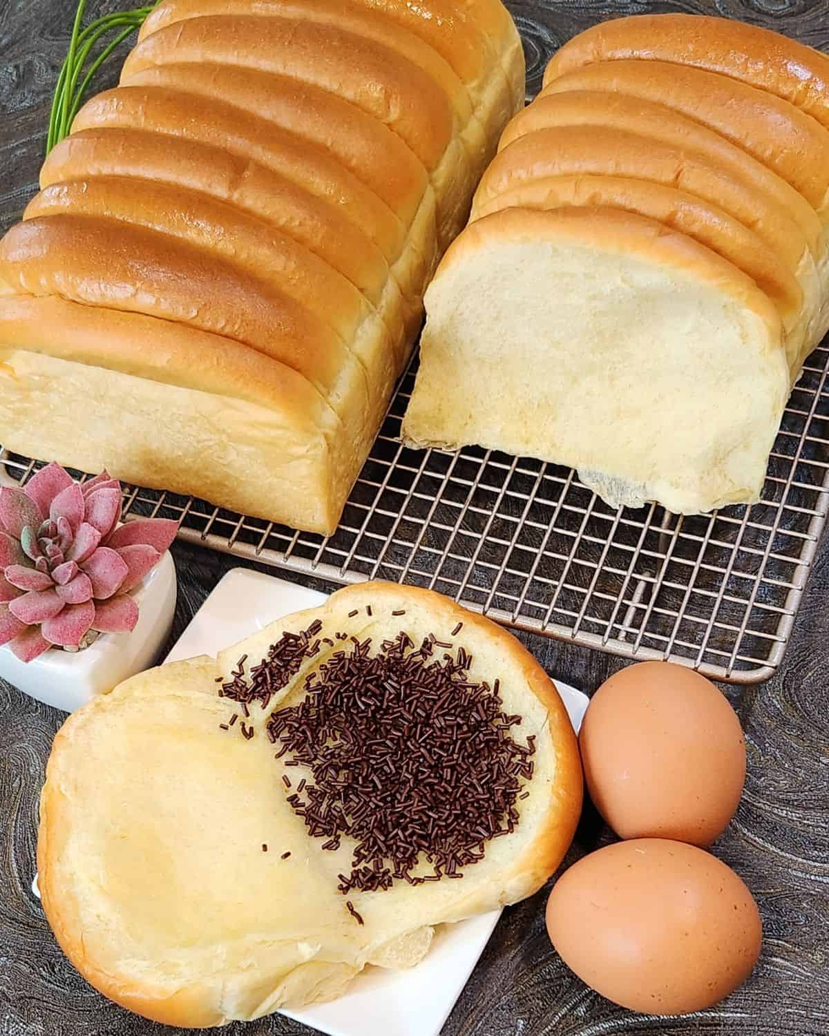 Two loaves of roti sisir on a cooling rack and a slice opened brushed with butter and sprinkled with chocolate.