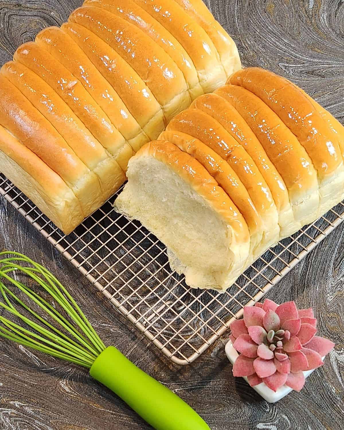 Two loaves of roti sisir on a cooling rack with a green whisk.