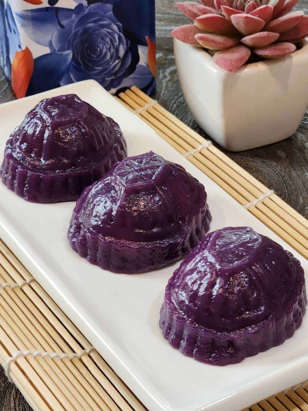 A plate of three angku kueh purple sweet potato on a bamboo tray.