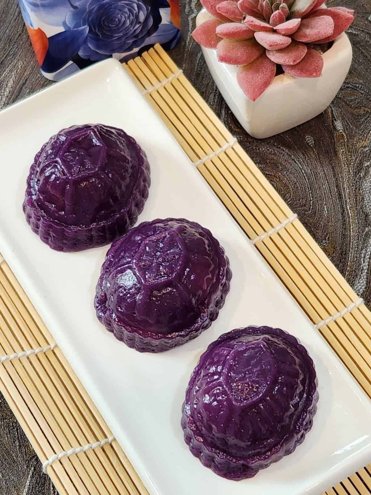 A plate of three angku kueh purple sweet potato on a bamboo tray.
