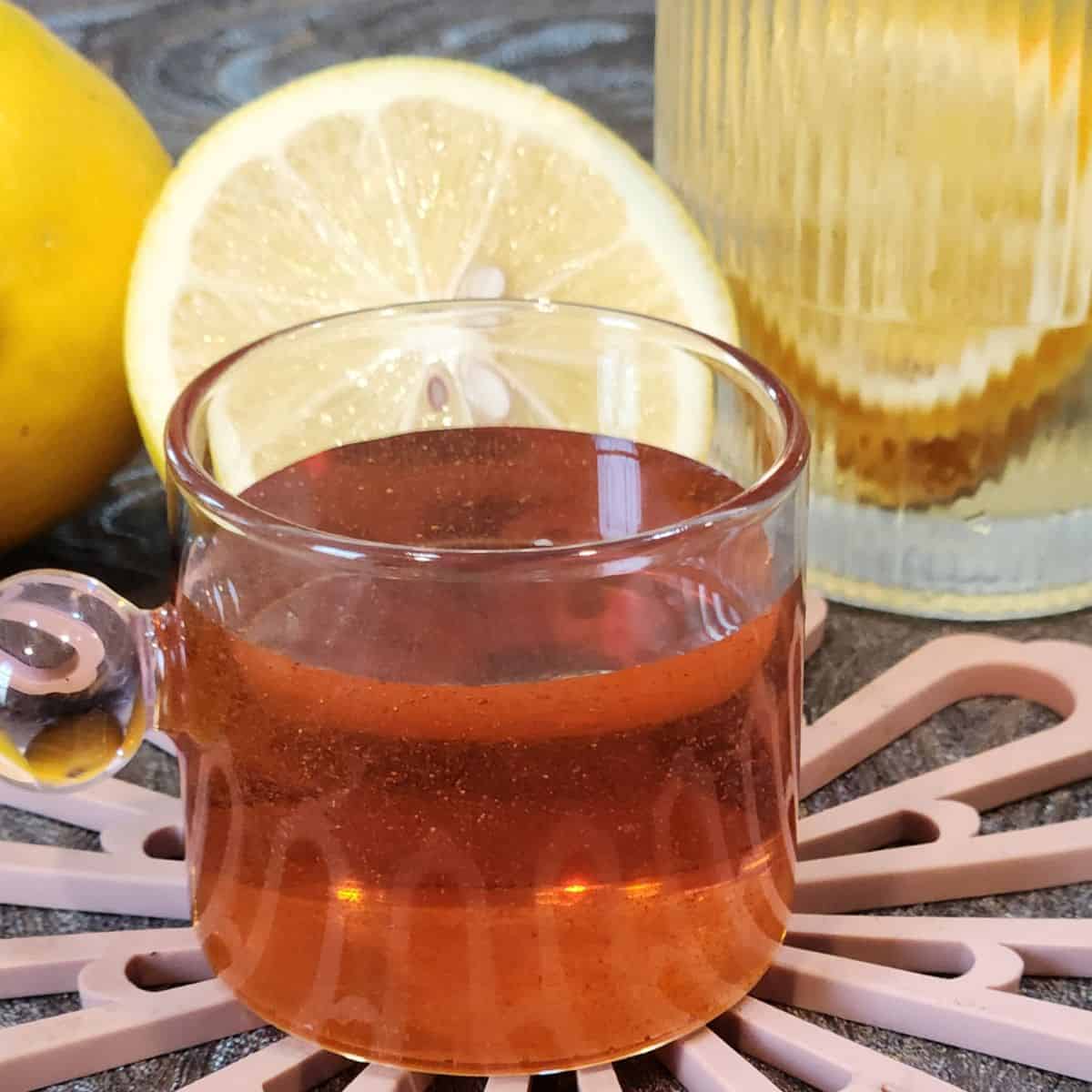 A small cup of homemade golden syrup with lemons on a table.