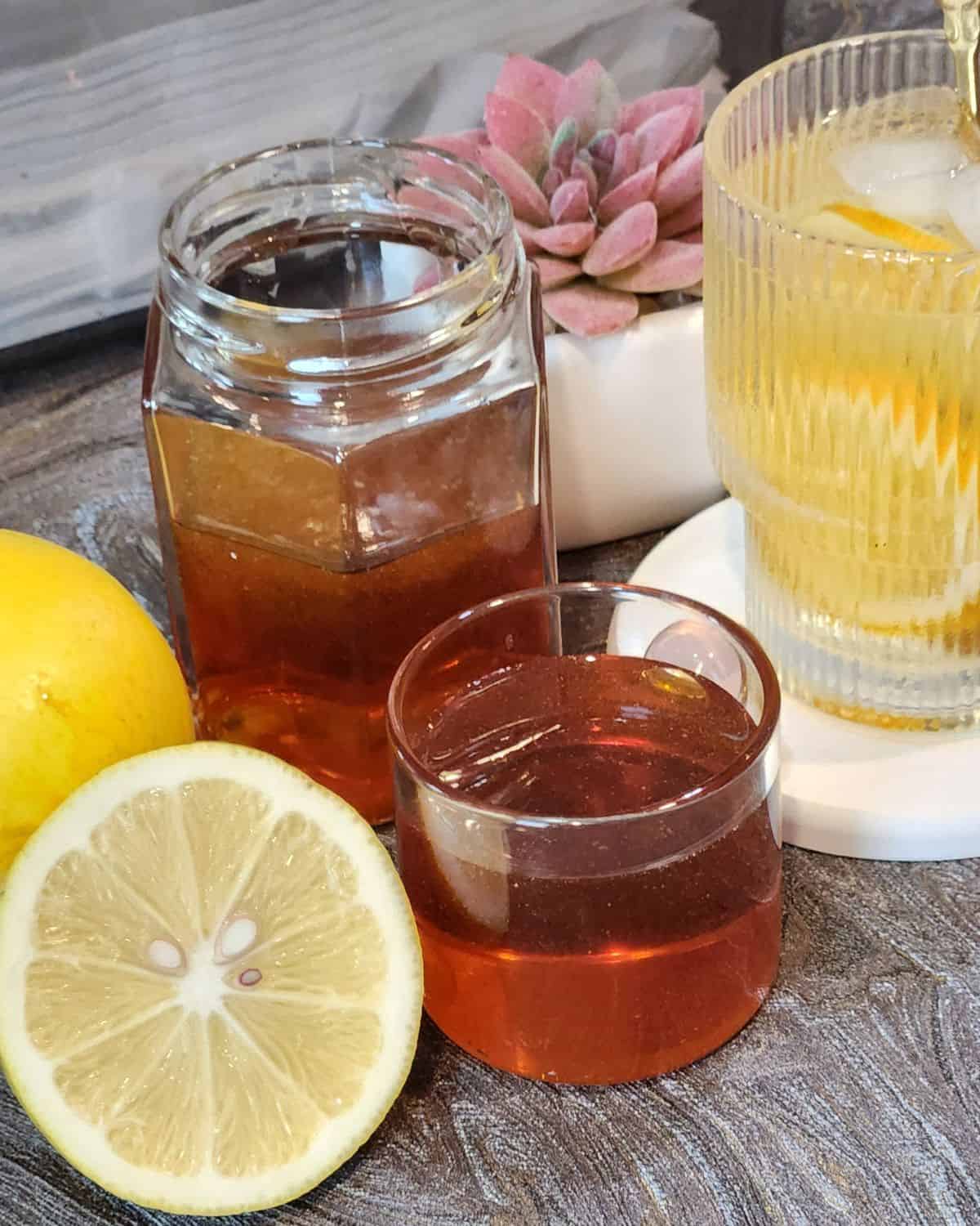 Homemade golden syrup recipe in a jar and in a small cup with some lemons on a table.