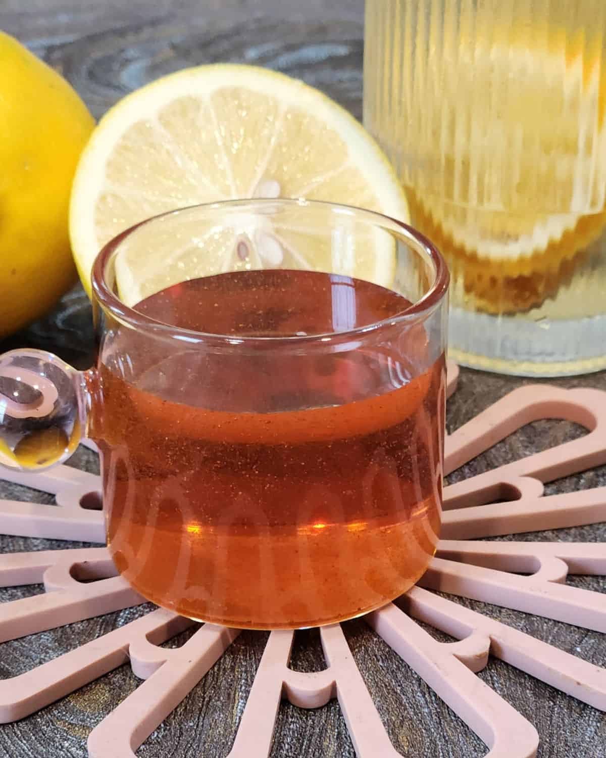 A small cup of homemade golden syrup with lemons on a table.