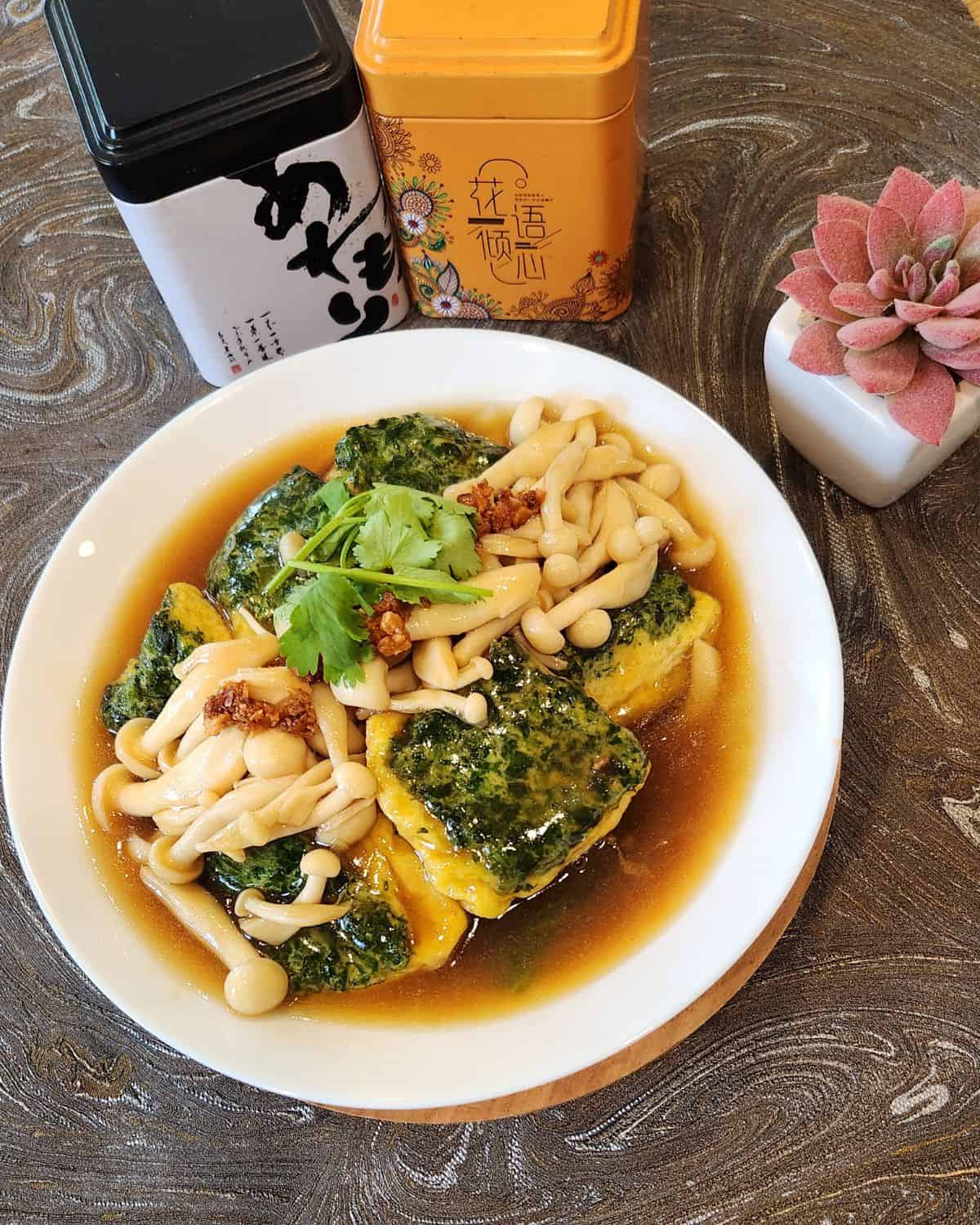 A plate of spinach tofu with shimeji mushrooms on top, garnished with coriander leaves.