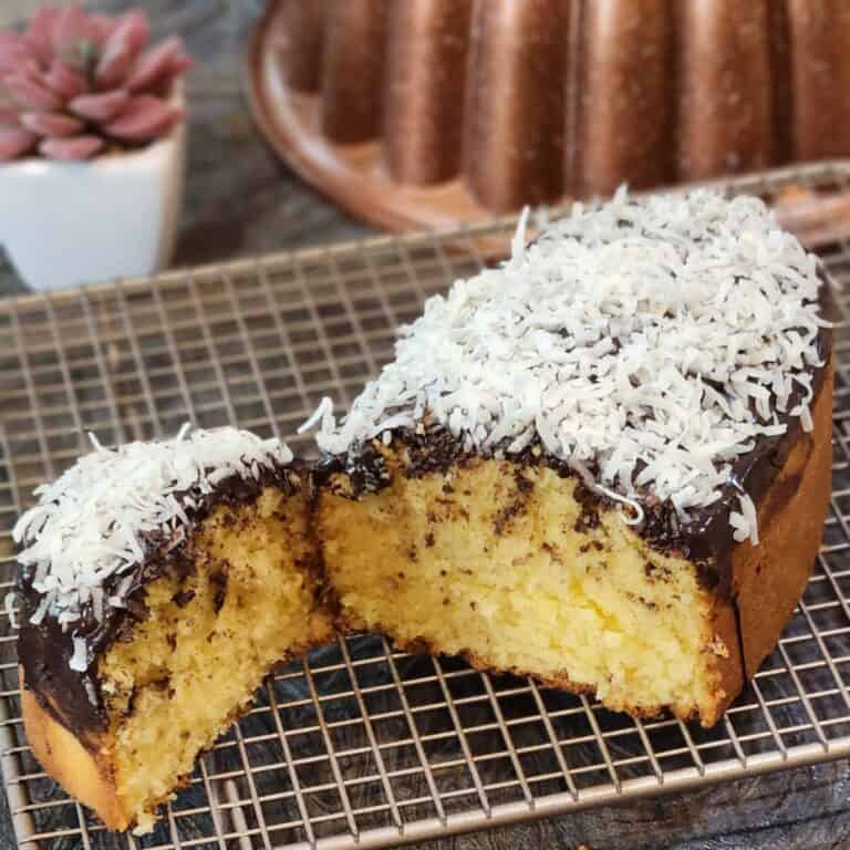 Coconut pound cake with chocolate glaze and coconut flakes on a wire rack.
