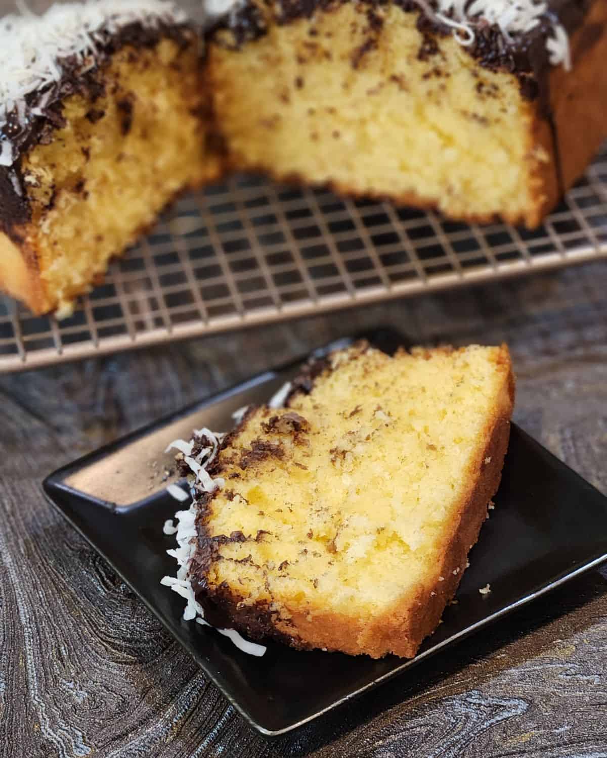 A slice of coconut pound cake with chocolate glaze and coconut flakes on a small plate.