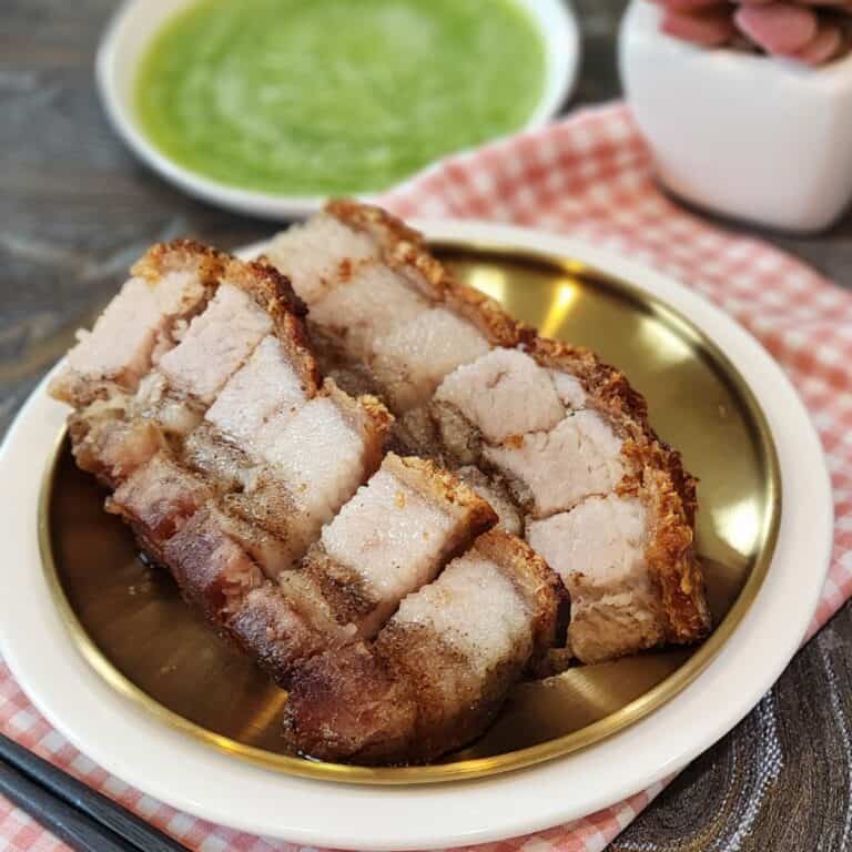 A small plate of neatly lined crispy pork belly with green chilis dipping sauce.