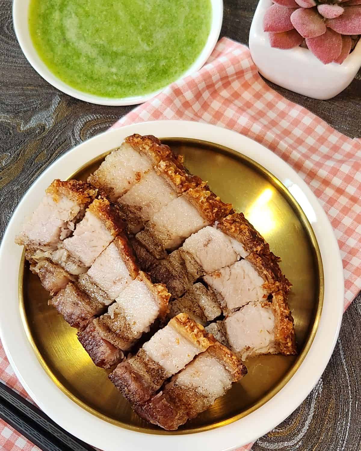 A small plate of neatly lined crispy pork belly with green chilis dipping sauce.