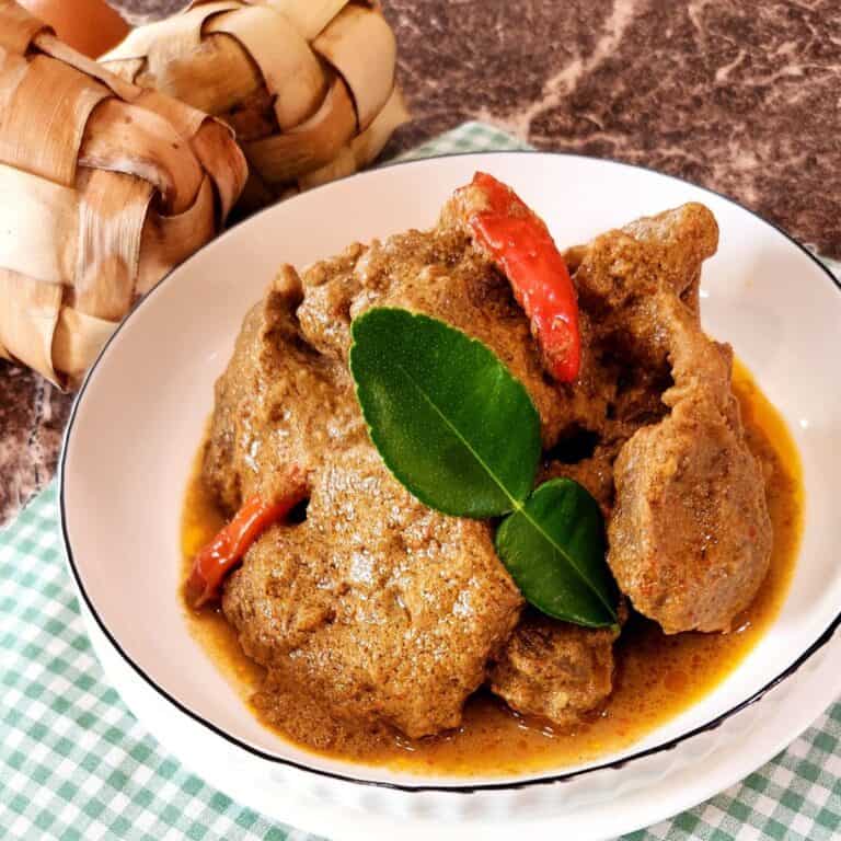 A few slices of Indonesian beef rendang on a white plate with chilis and lime leaf.