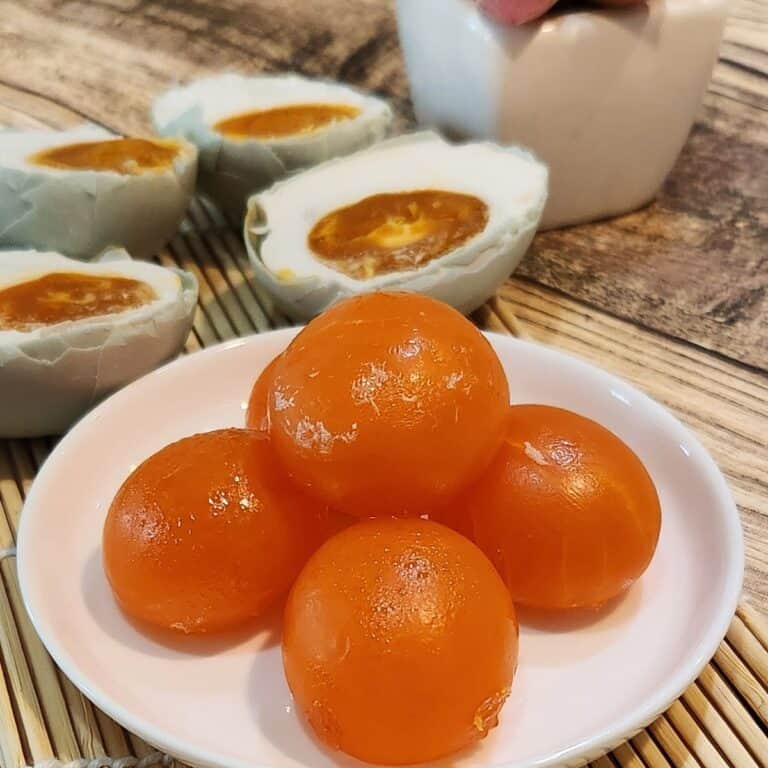 A stack of salted egg yolks on a white plate with cooked salted duck egg yolks at the back.