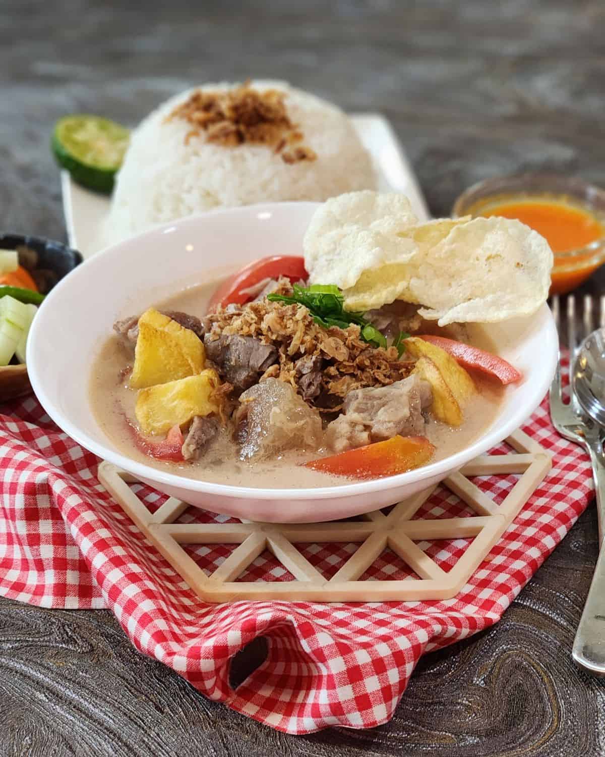 A bowl of Soto Betawi with white rice, chili sauce, and acar timun.
