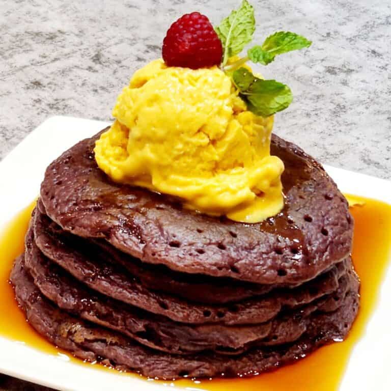 A stack of ube mochi pancakes drizzled with maple syrup and topped with mango ice cream.