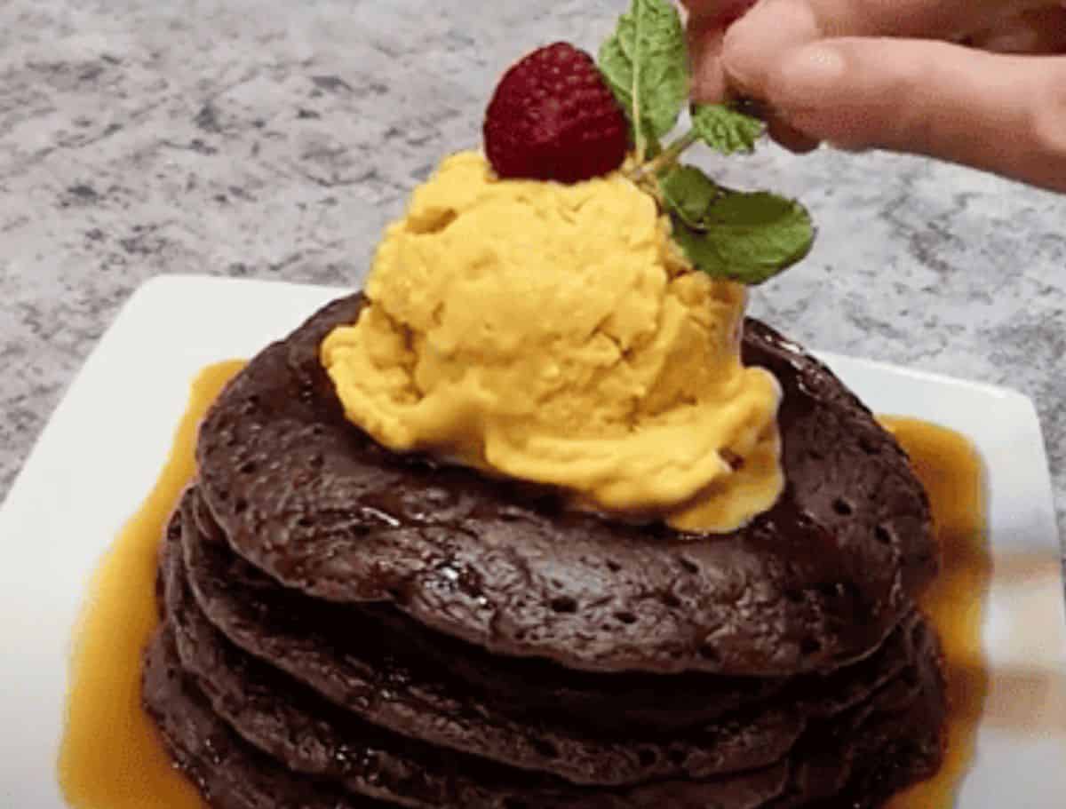 A stack of ube mochi pancakes drizzled with maple syrup and topped with mango ice cream.