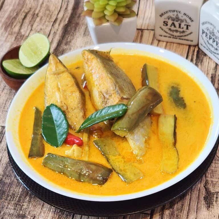 A bowl of fish curry with lime wedges on the side.