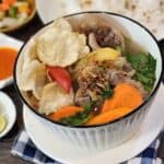A bowl of Indonesian oxtail soup with emping crackers and fried shallots.