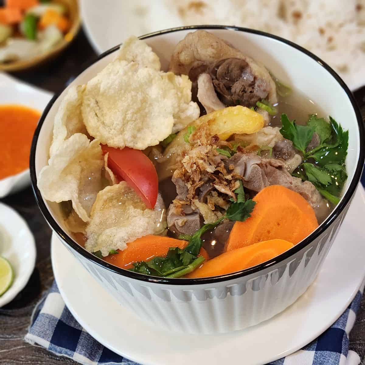 A bowl of Indonesian oxtail soup with emping crackers and fried shallots.