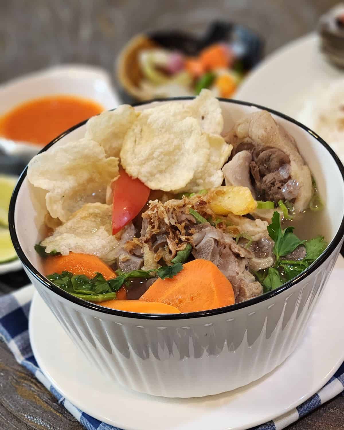 A bowl of oxtail soup or sop buntut with emping crackers.